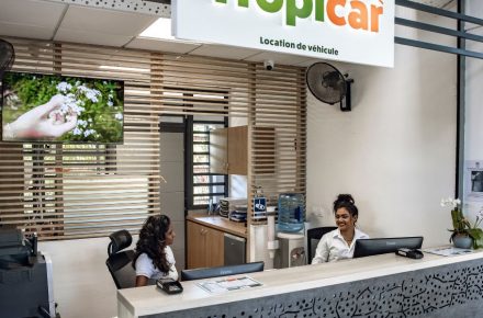 Photographie d'un comptoir de location de voiture à l'aéroport Roland Garros de La Réunion, montrant deux hotesses d'accueil souriantes et accueillantes prêtes à renseigner les clients